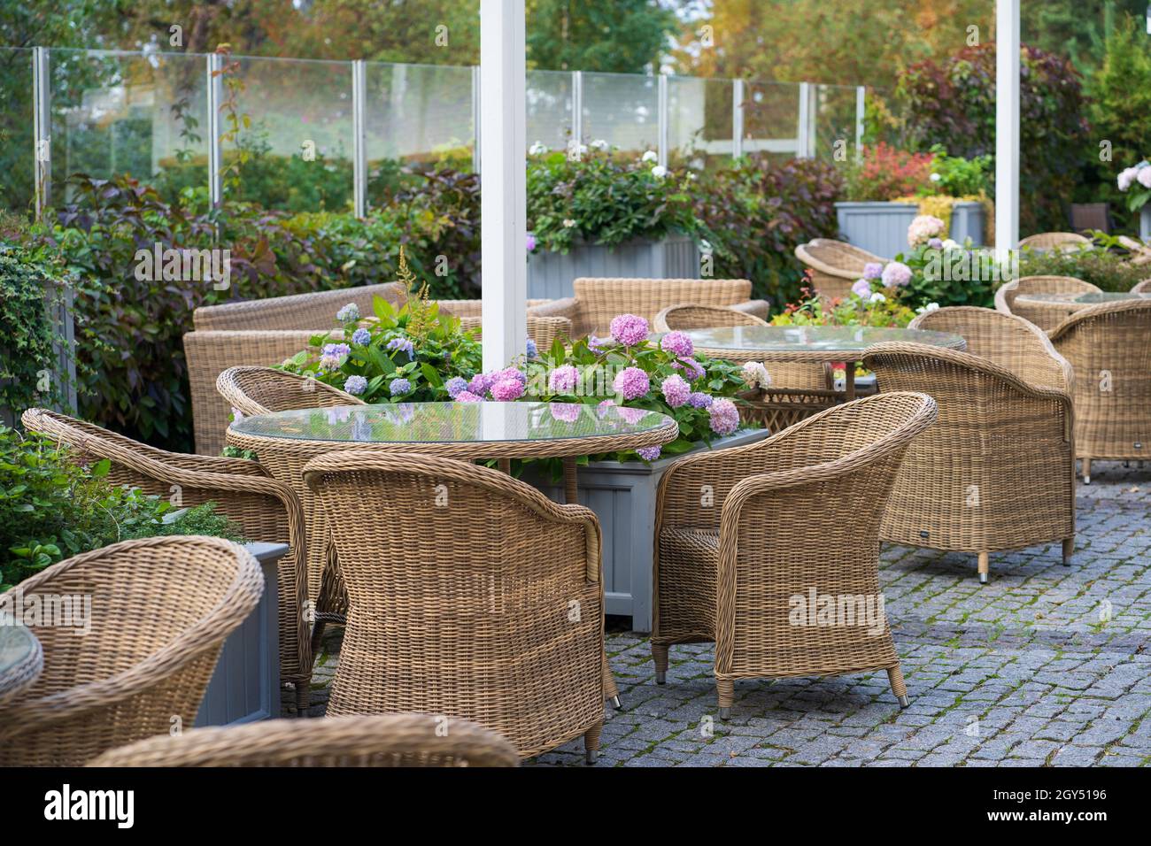 Leere Außencafe-Terrasse mit Korbmöbeln und wachsenden Blumen im Topf für die Sommerunterhaltung Stockfoto