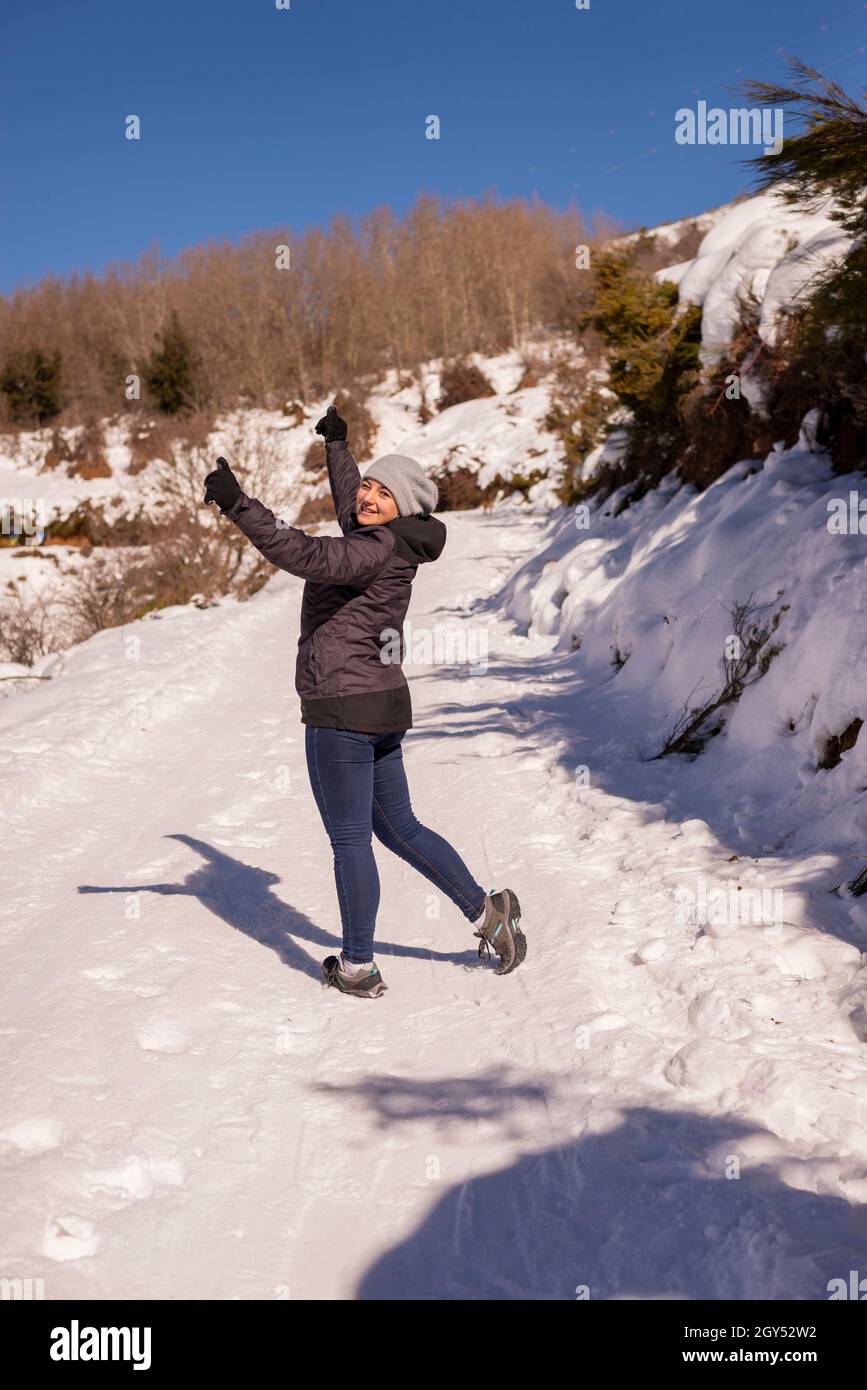 Eine junge Reisende Frau, die mit erhobenen Armen auf einem Schneeberg steht Stockfoto
