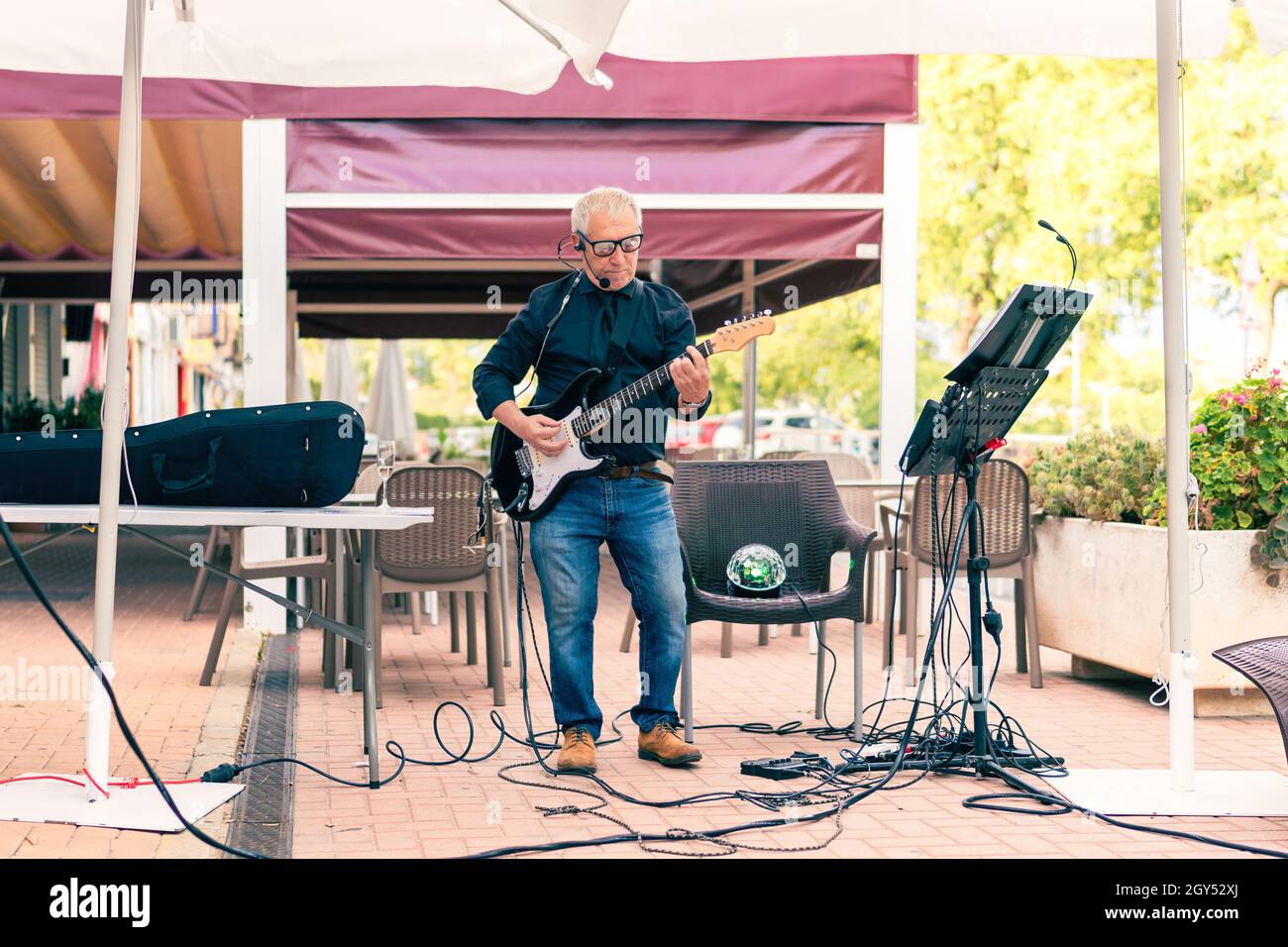 Gealterter Musiker, der auf einer Terrasse mit Publikum die E-Gitarre spielt Stockfoto