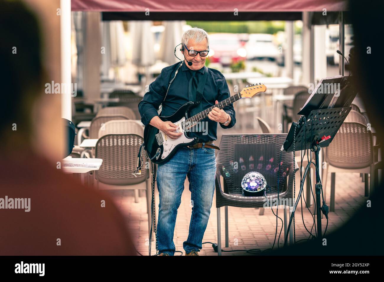 Älterer Musiker, der auf einer Terrasse mit Publikum die E-Gitarre spielt Stockfoto