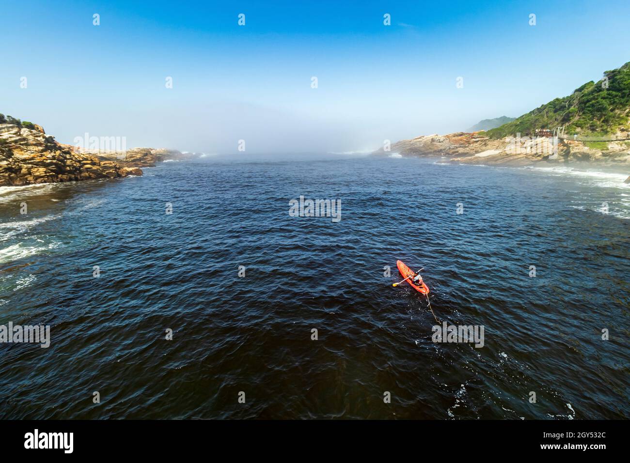 Ein eingängiger Kajakfahrer paddelt im Wasser der Stürme in Richtung Nebelmeer entlang der Flussmündung des Tsitsikamma National Park an der Garden Route in Südafrika. Stockfoto