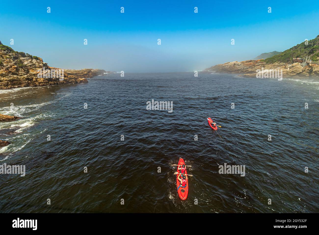 Drei Kajakfahrer paddeln im Wasser der Stürme in Richtung Nebelmeer Flussmündung des Tsitsikamma National Park auf der Garden Route in Südafrika. Stockfoto