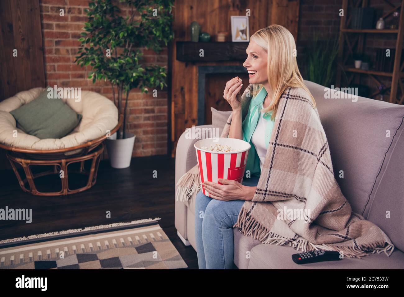 Porträtfoto Frau, die zu Hause auf dem Sofa Fernsehen und Popcorn isst, lacht zu Hause glücklich Stockfoto
