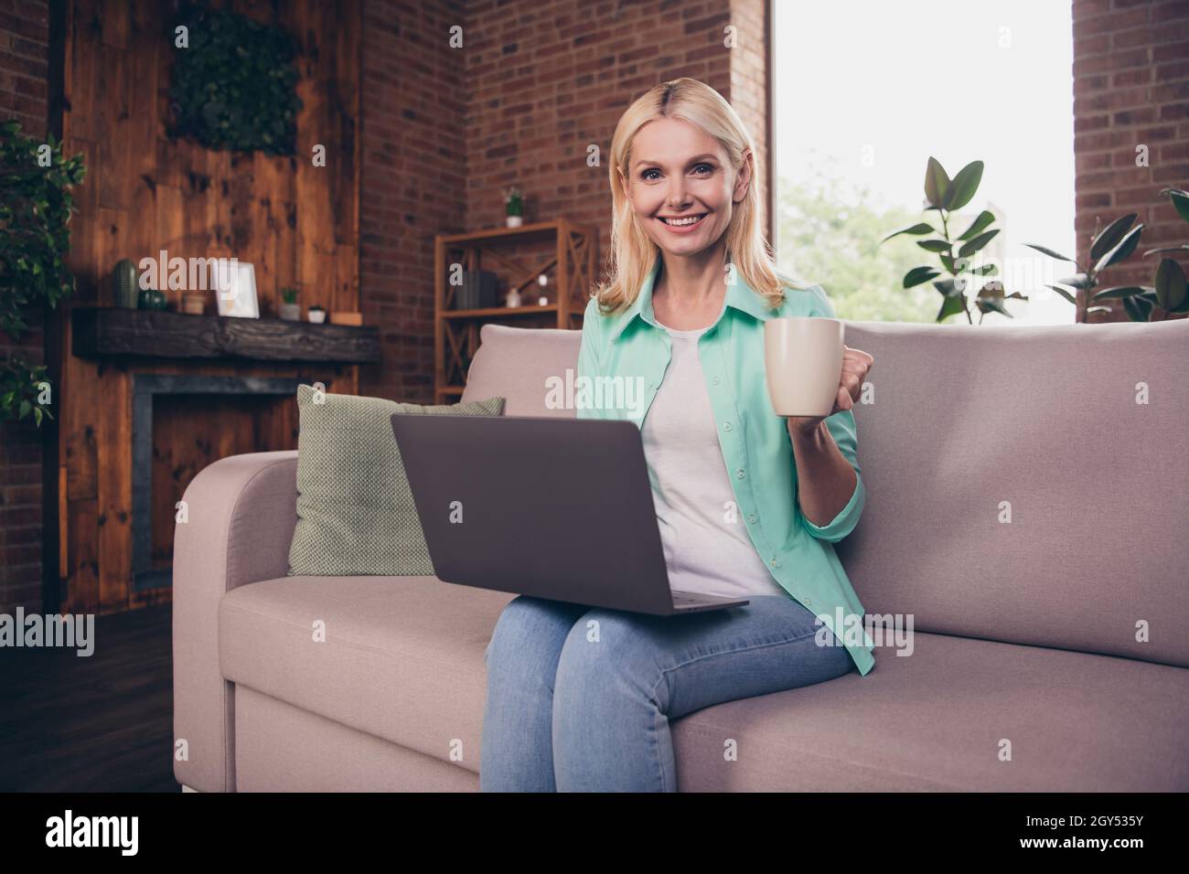 Porträtfoto Frau lächelt am Computer zu Hause, trinkt Tee und verbringt Freizeit Stockfoto
