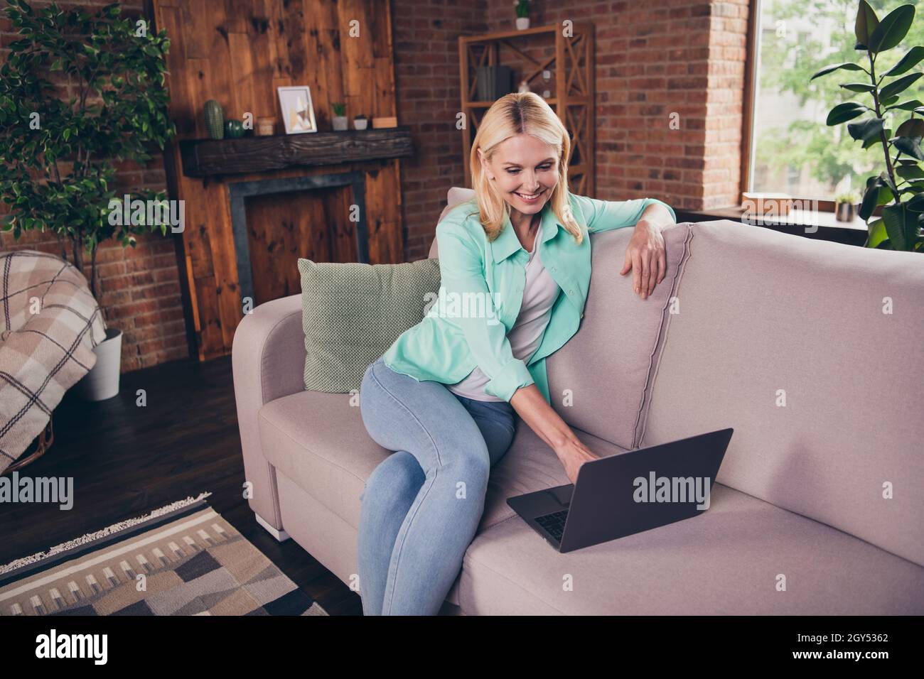 Porträtfoto Frau lächelt am Computer und schaut sich Videos auf dem Sofa an, die gute Laune haben Stockfoto