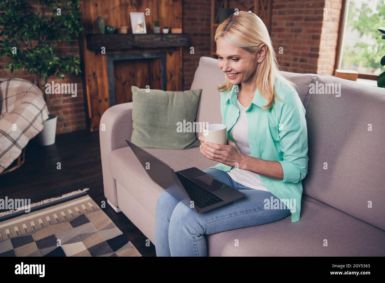 Portrait Foto Frau lächelnd mit Computer sitzen auf der Couch trinken Kaffee im Internet surfen Stockfoto