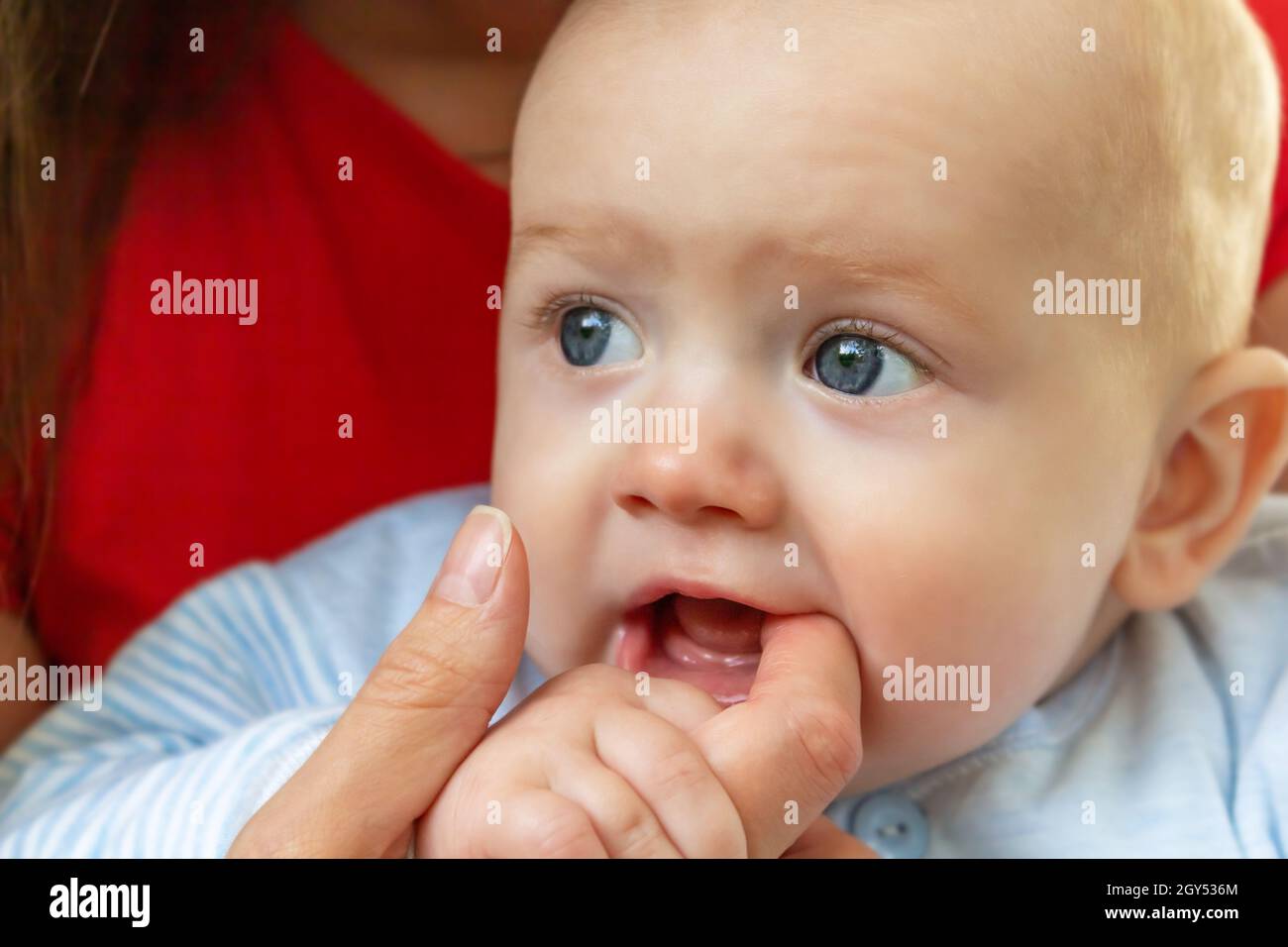Kleines Baby, das den Finger der Mutter im Mund hält. Stockfoto