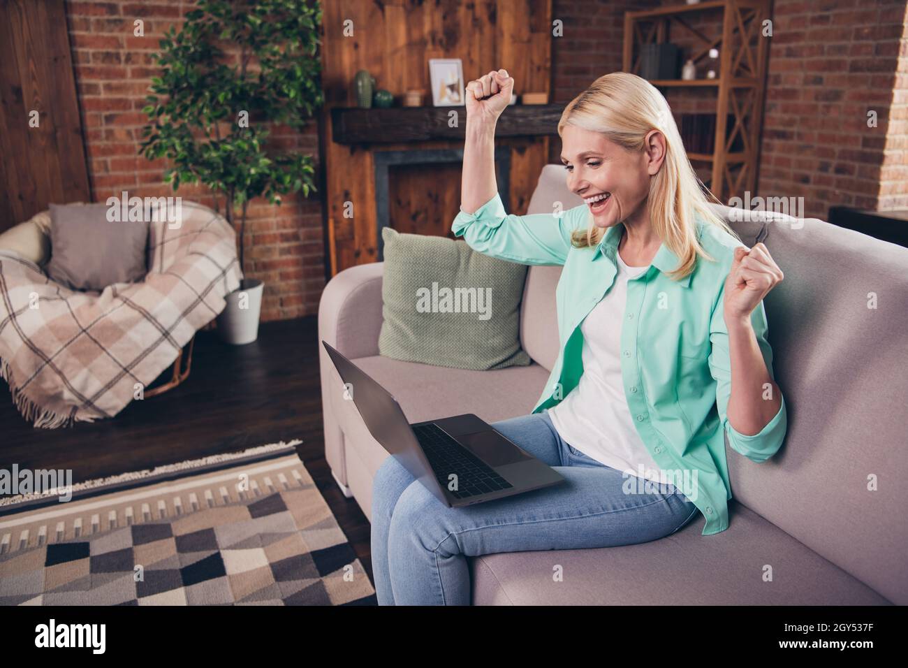 Porträtfoto Frau lächelt mit Laptop gestikulieren wie Gewinner glücklich überglücklich sitzen auf dem Sofa Stockfoto
