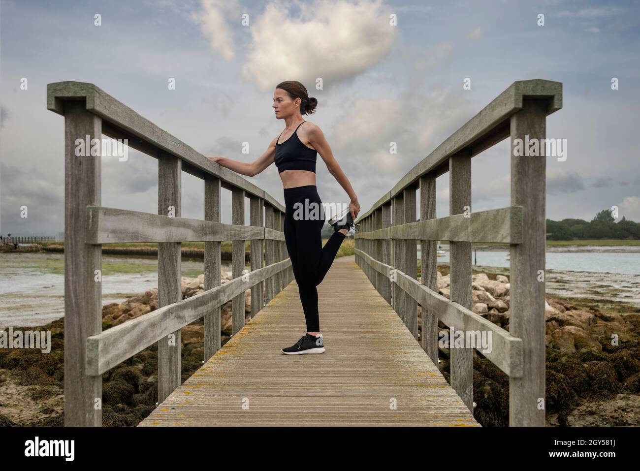 Fit, sportliche Frau macht Bein Stretch Warm-up-Übungen draußen auf einer Holzbrücke. Stockfoto