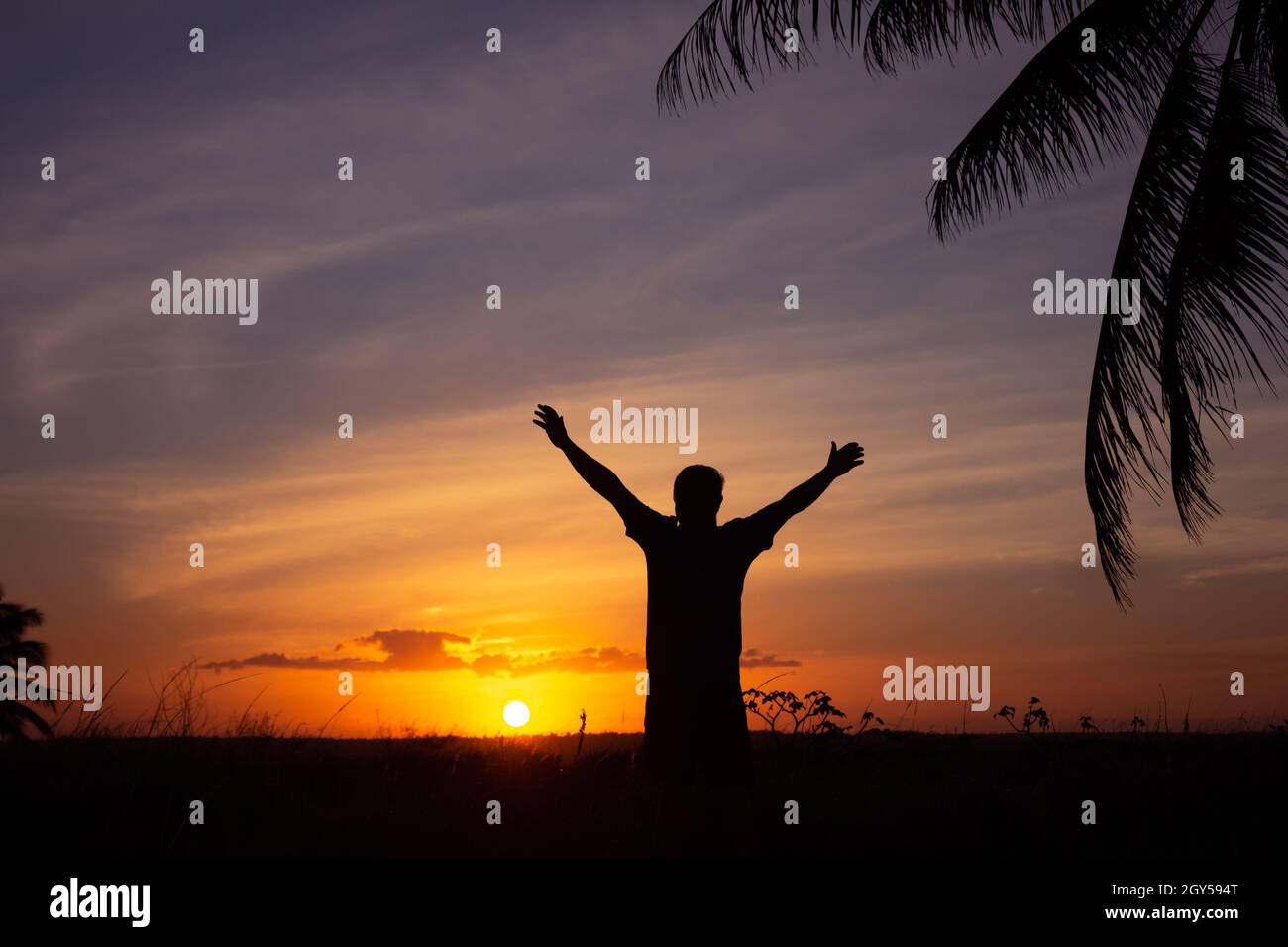 Silhouette eines erwachsenen Mannes mit ausgestreckten Armen in einer Haltung des Glücks. Glücklicher Mann bei Sonnenuntergang. Urlaubslandschaft. Stockfoto