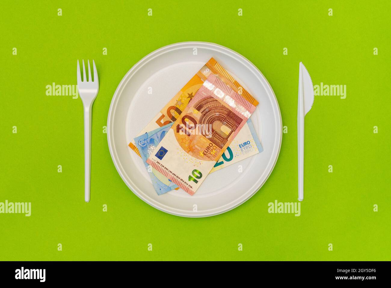 Draufsicht auf Einwegbesteck und Teller mit Euro-Scheinen. Lebensmittelkosten. Stockfoto