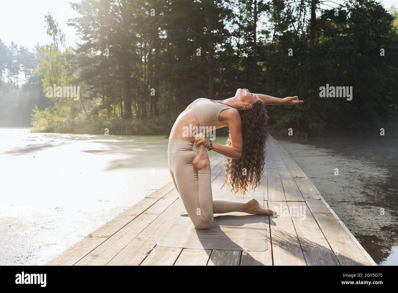 Frau in Sportbekleidung praktiziert Yoga, führt Ushtrasana Übung mit Virasana, Kamel und Held Pose, Training im Freien im Park auf einem sonnigen mor Stockfoto
