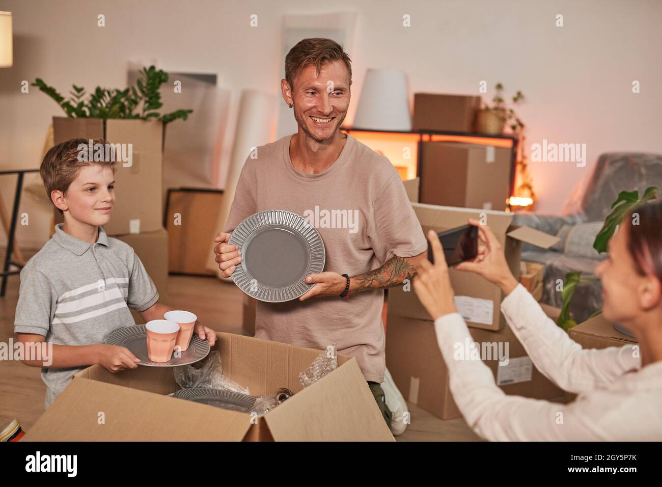 Porträt einer jungen glücklichen Familie, die Boxen auspackt und Fotos macht, während sie in ein neues Zuhause einzieht und Platz kopiert Stockfoto