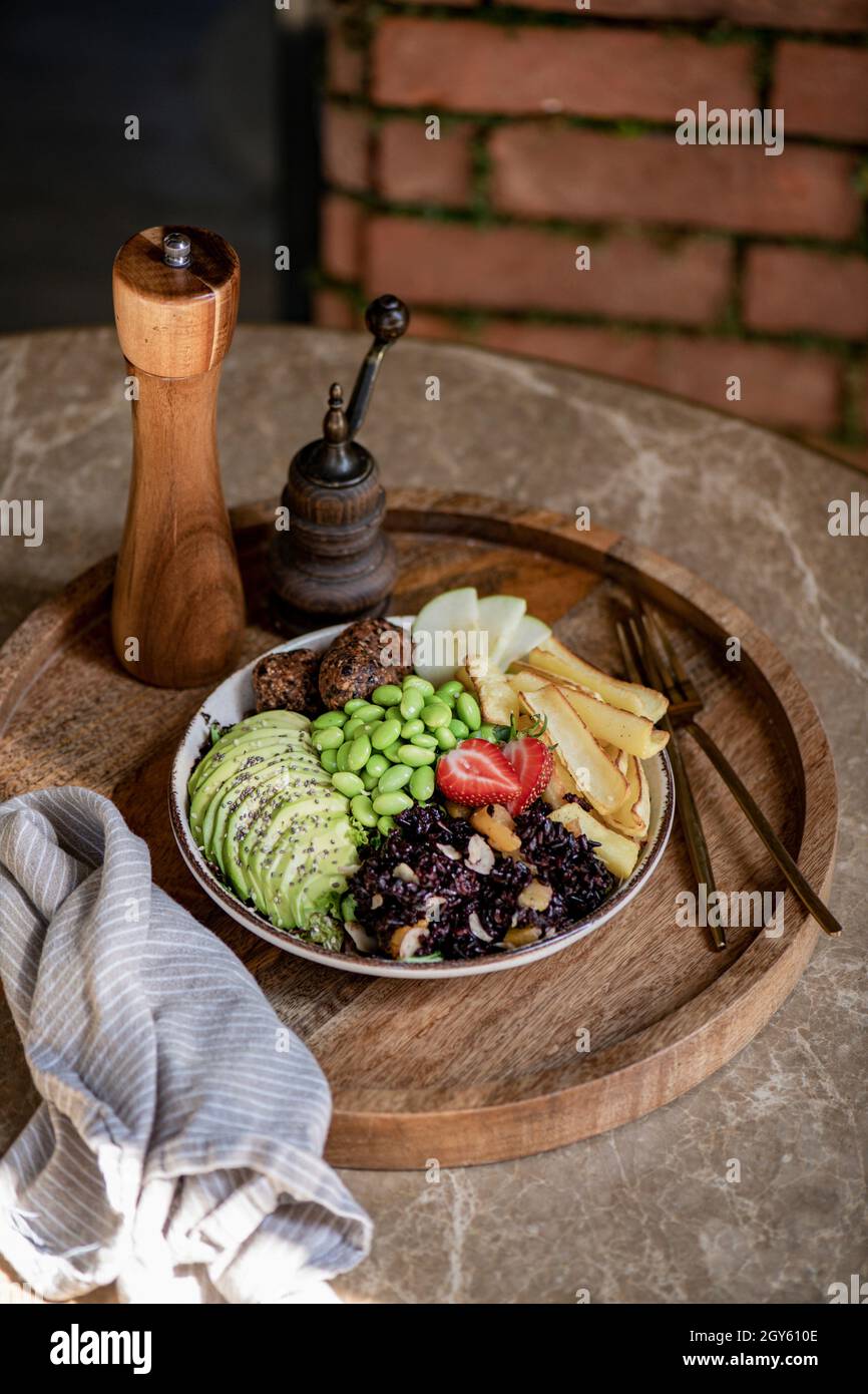 Gesunde vegane Falafel, Edamame, Avocado und brauner Reis Frühstück oder Mittagessen Schüssel auf Holztablett über Marmortisch. Sauberes Essen, Fitness, Vegetarier, wir Stockfoto