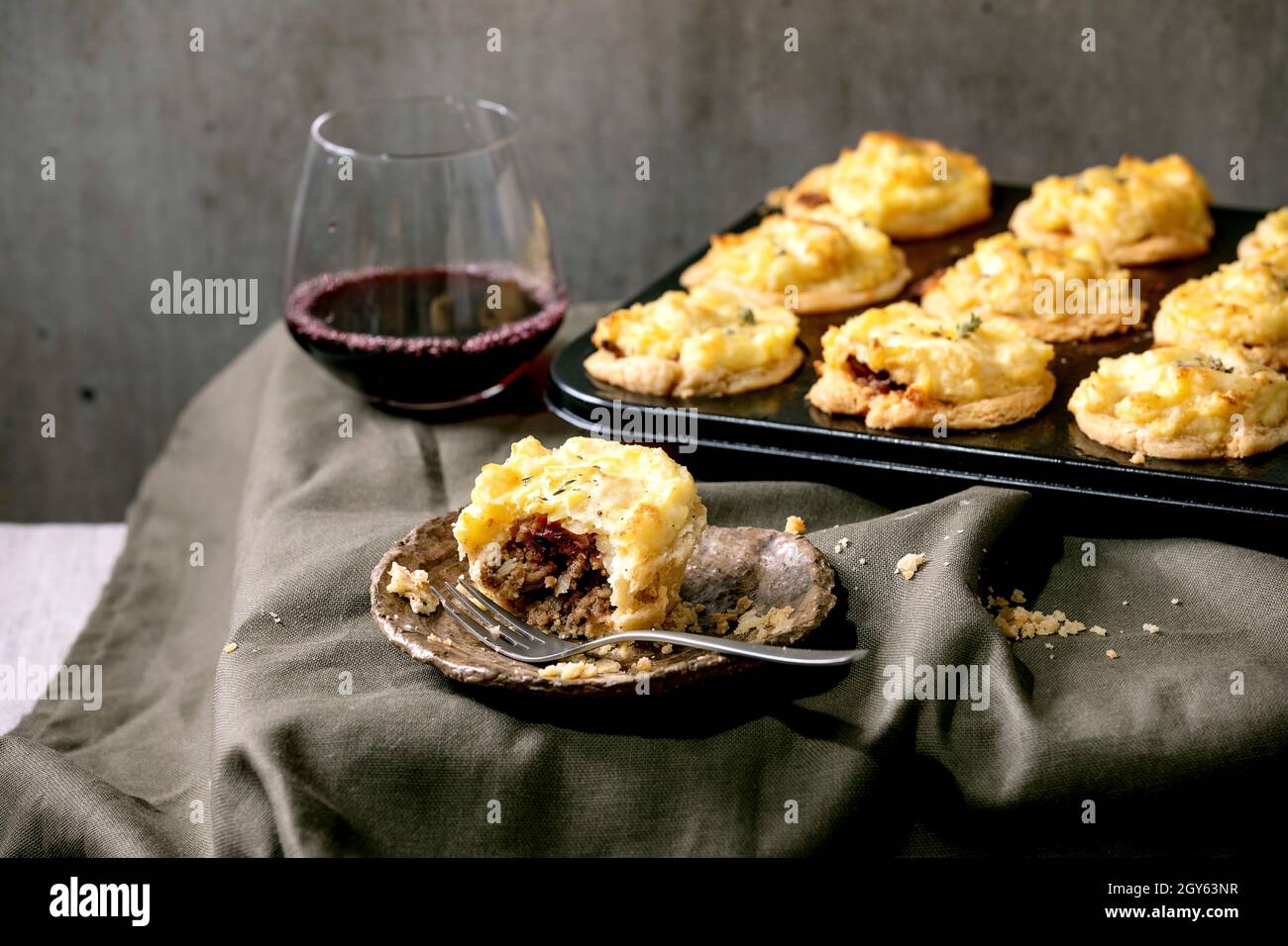 Ganze und beginnen zu essen hausgemachte Mince Fleisch Mürbeteig Mini-Kuchen mit Kartoffelpüree und Thymian in schwarzem Backblech und ein Glas Rotwein. Dar Stockfoto