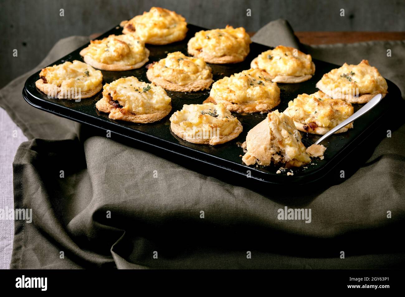 Hackfleisch Mürbeteig Mini-Pasteten mit Kartoffelpüree und Thymian in schwarzem Backblech. Dunkle Tischdecke aus Leinen, graue Wand im Hintergrund. Abendessen zu Hause Stockfoto