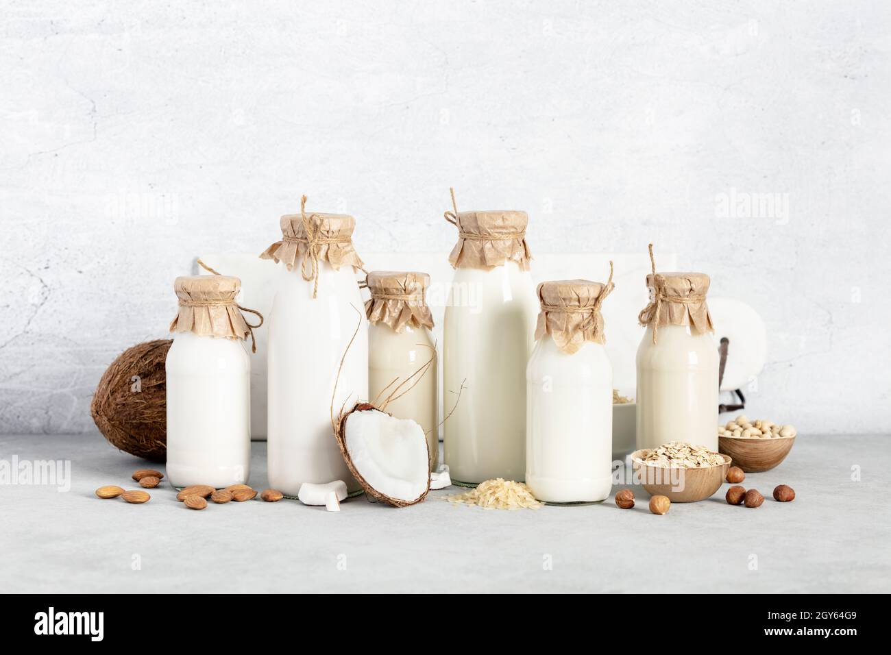 Vegane Milch auf pflanzlicher Basis ohne Milchprodukte in Flaschen und Zutaten auf hellem Hintergrund (Mandel, Haselnuss, Reis, Hafer, Soja). Alternative laktosefreie Milch subs Stockfoto