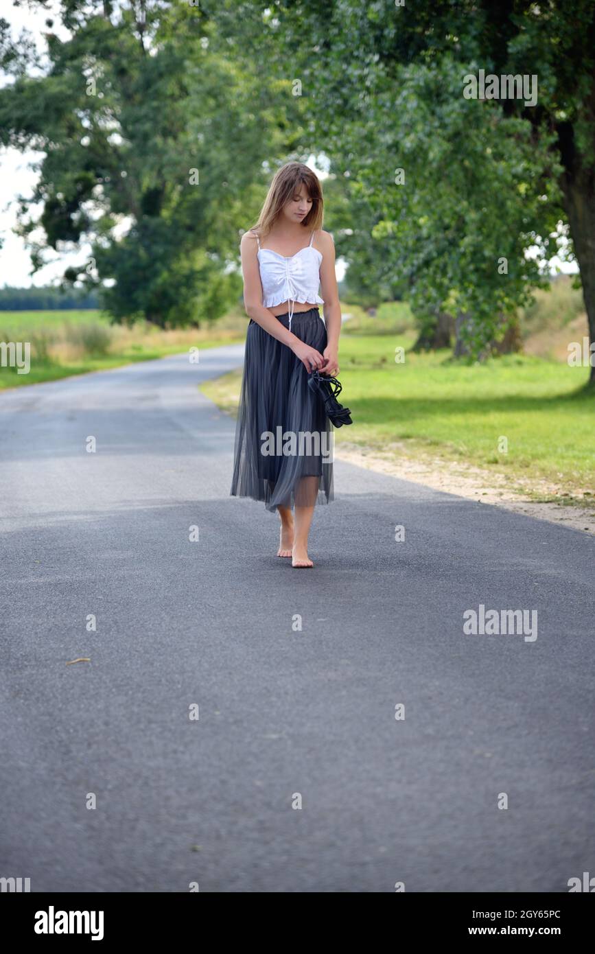 Außenfotos einer jungen Frau in den 30er Jahren. Sommersaison in Polen.  Frau, die barfuß auf leerer Straße geht Stockfotografie - Alamy