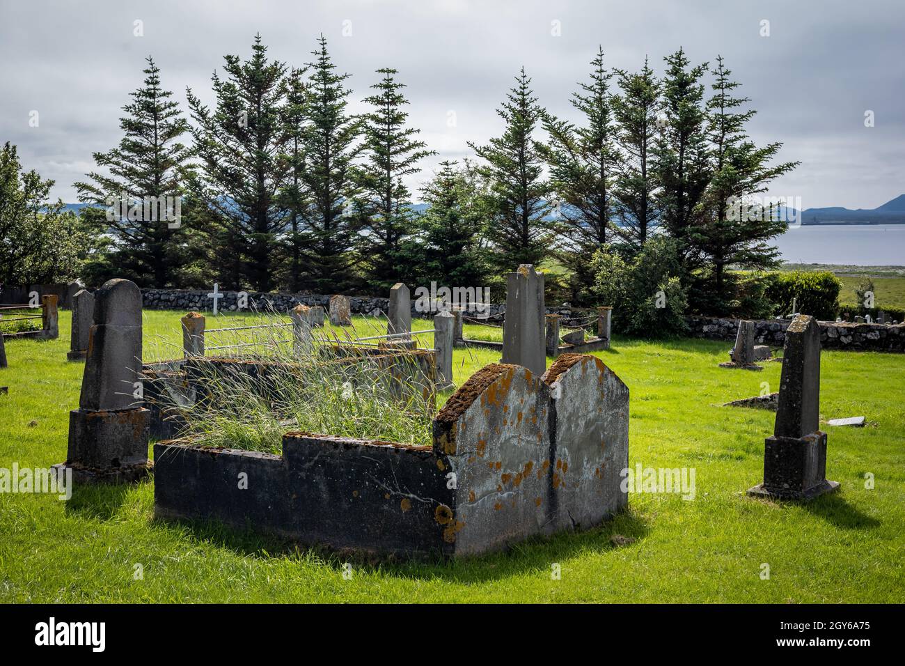 Ein altes, verlassene Doppelgrab auf dem Friedhof, umgeben von kleineren Grabsteinen. Grünes Gras, Bäume im Hintergrund. Stockfoto