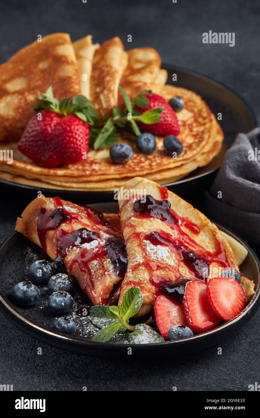 Pfannkuchen mit Beeren und süßer Sauce auf schwarzem Hintergrund. Maslenitsa. Shrovetide. Faschingsdienstag. Pfannkuchen-Tag. Frohe Festtage, Grüße. Nachtisch. Se Stockfoto