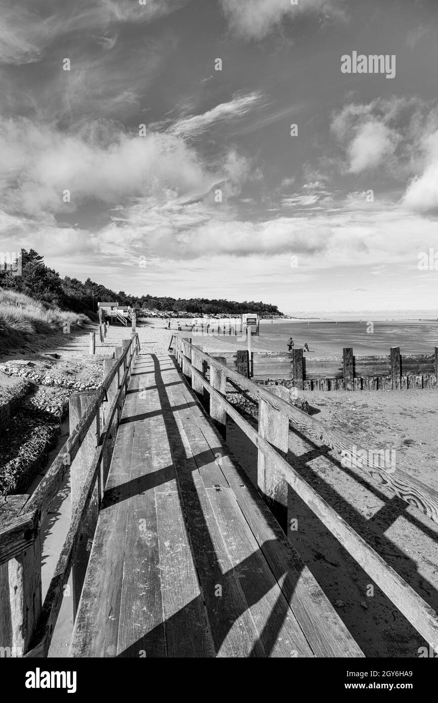 Promenade, die zu Strand- und Strandhütten führt, mit Blick auf die Holkham Bay im Well-Next-the-Sea an einem hellen und sonnigen Oktobermorgen in Monochrom Stockfoto