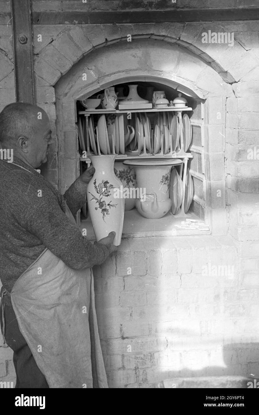 Ein Keramiker der Staatlichen Porzellanmanufaktur Berlin stellt eine bemalte Vase in den Brennofen für den Glattbrand, Deutschland 1930er Jahre. Keramikerin der Staatlichen Porzellanmanufaktur Berlin setzt eine bemalte Vase im Brennofen für die glost Feuern, Deutschland 1930. Stockfoto