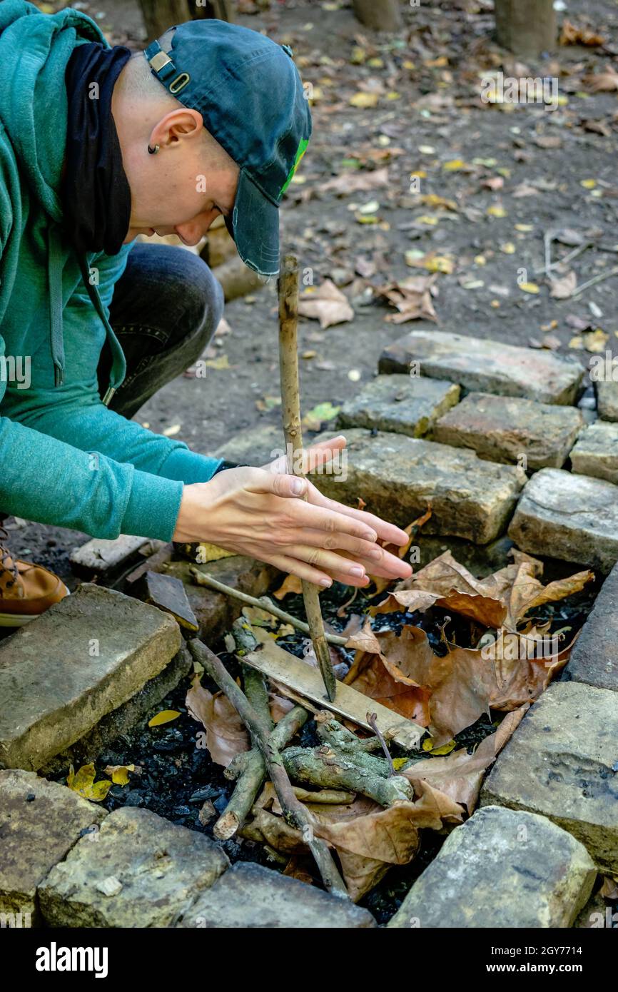 Mann, der ein Feuer für den Grill im Wald mit einer Technik der Reibung. Mit primitiven Werkzeugen überleben Handwerk und Fähigkeiten üben. Stockfoto