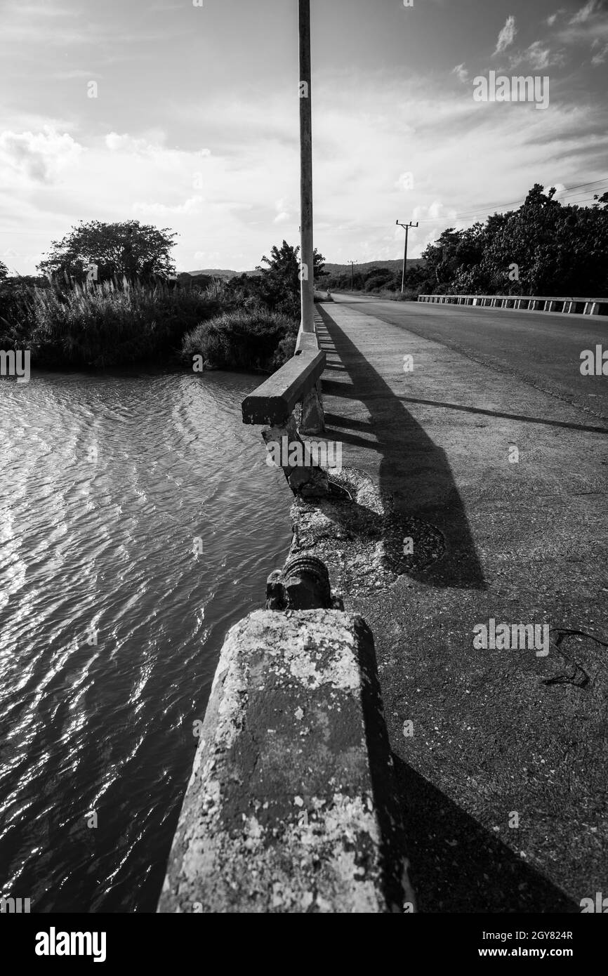 Eine symmetrische Ansicht schwarz und weiß von einem Fluss und der Brücke Seite an Seite, mit der Schiene gebrochen und starkes Sonnenlicht umgeben von der unberührten Natur. Stockfoto