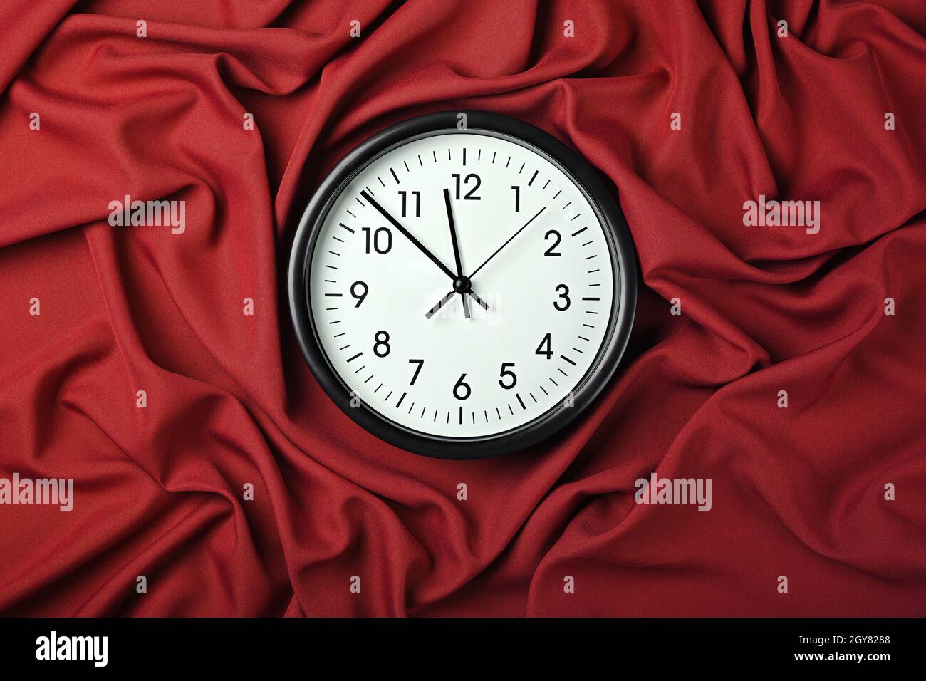 Close up weiße Wand klassische Uhr über roten Textil-Hintergrund mit gefalteten Falten aus Stoff, erhöhte Ansicht von oben, direkt darüber Stockfoto