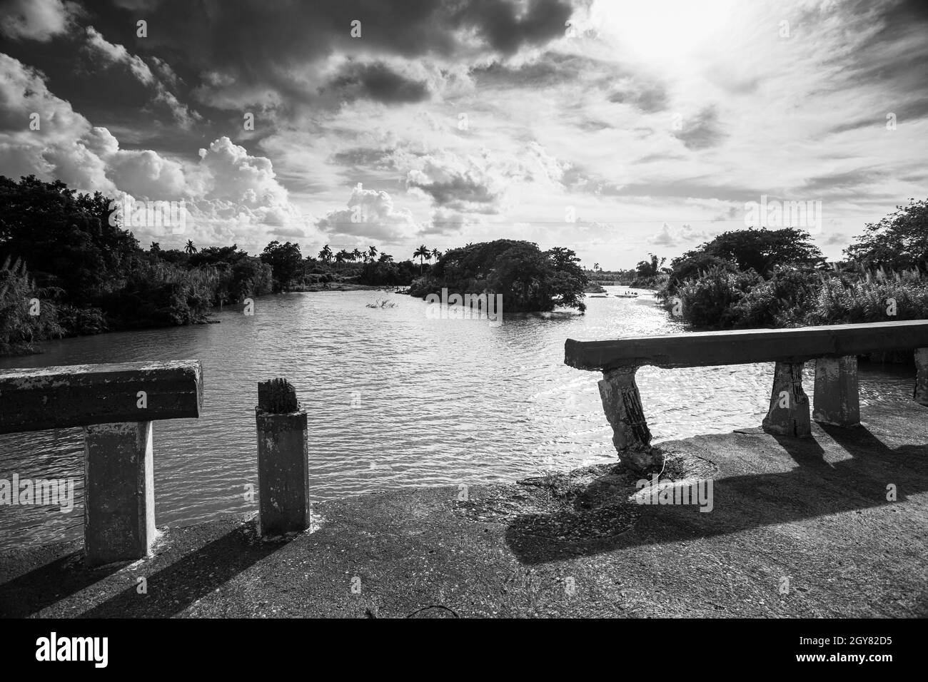 Eine Symmetrie Blick schwarz und weiß von einem Fluss und der Brücke, mit der Schiene gebrochen und starkes Sonnenlicht umgeben von der unberührten Natur. Stockfoto