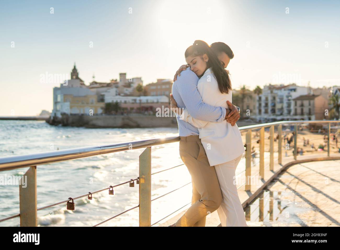 Seitenansicht des zarten hispanischen Paares, das sich umarmt, während es an sonnigen Tagen in der Nähe des Geländers auf der Promenade gegen das Meer steht Stockfoto