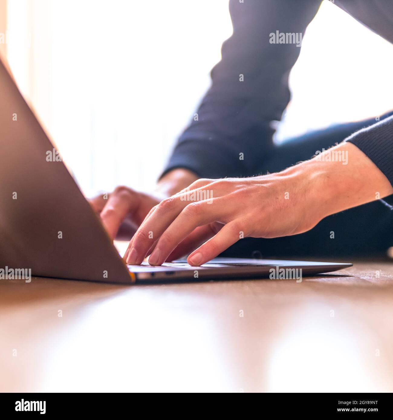 Junger Mann mit einem Laptop arbeitet auf dem Holzboden, Licht aus dem Fenster kommt Stockfoto
