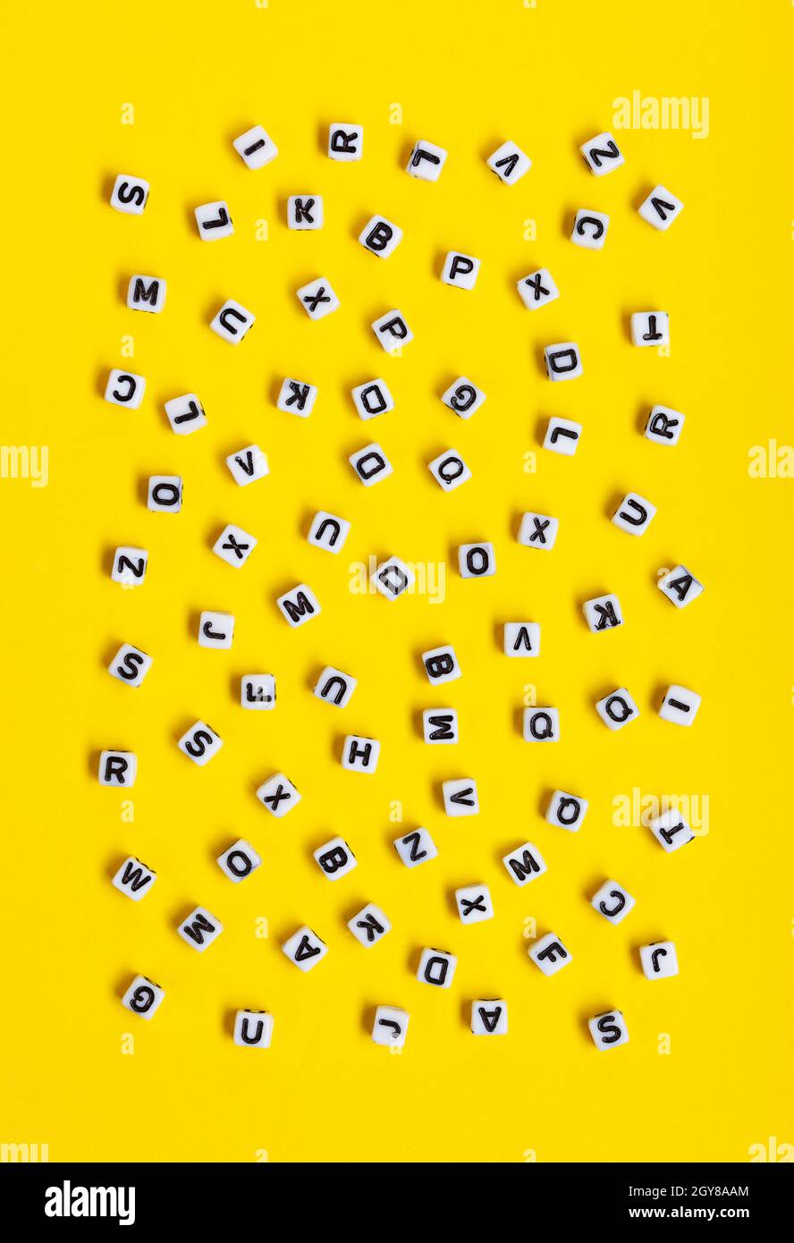 Weiße Würfel mit zufällig auf gelbem Hintergrund verstreuten Buchstaben. Das Bild kann für viele Zwecke, Buchumschläge oder Konzepte zum Gramm verwendet werden Stockfoto