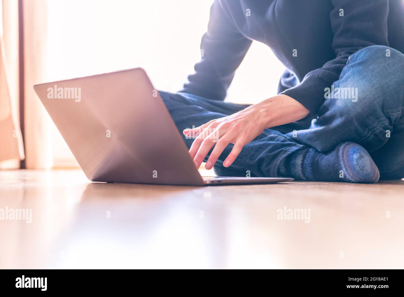 Junger Mann mit einem Laptop arbeitet auf dem Holzboden, Licht aus dem Fenster kommt Stockfoto