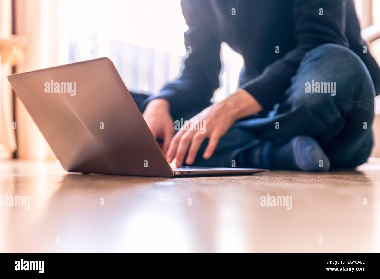 Junger Mann mit einem Laptop arbeitet auf dem Holzboden, Licht aus dem Fenster kommt Stockfoto