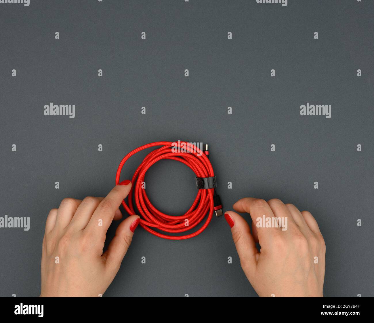 Die weibliche Hand hält verdrilltes Kabel zum Laden von mobilen Geräten in einer roten Textilverpackung auf schwarzem Hintergrund, Nahaufnahme Stockfoto