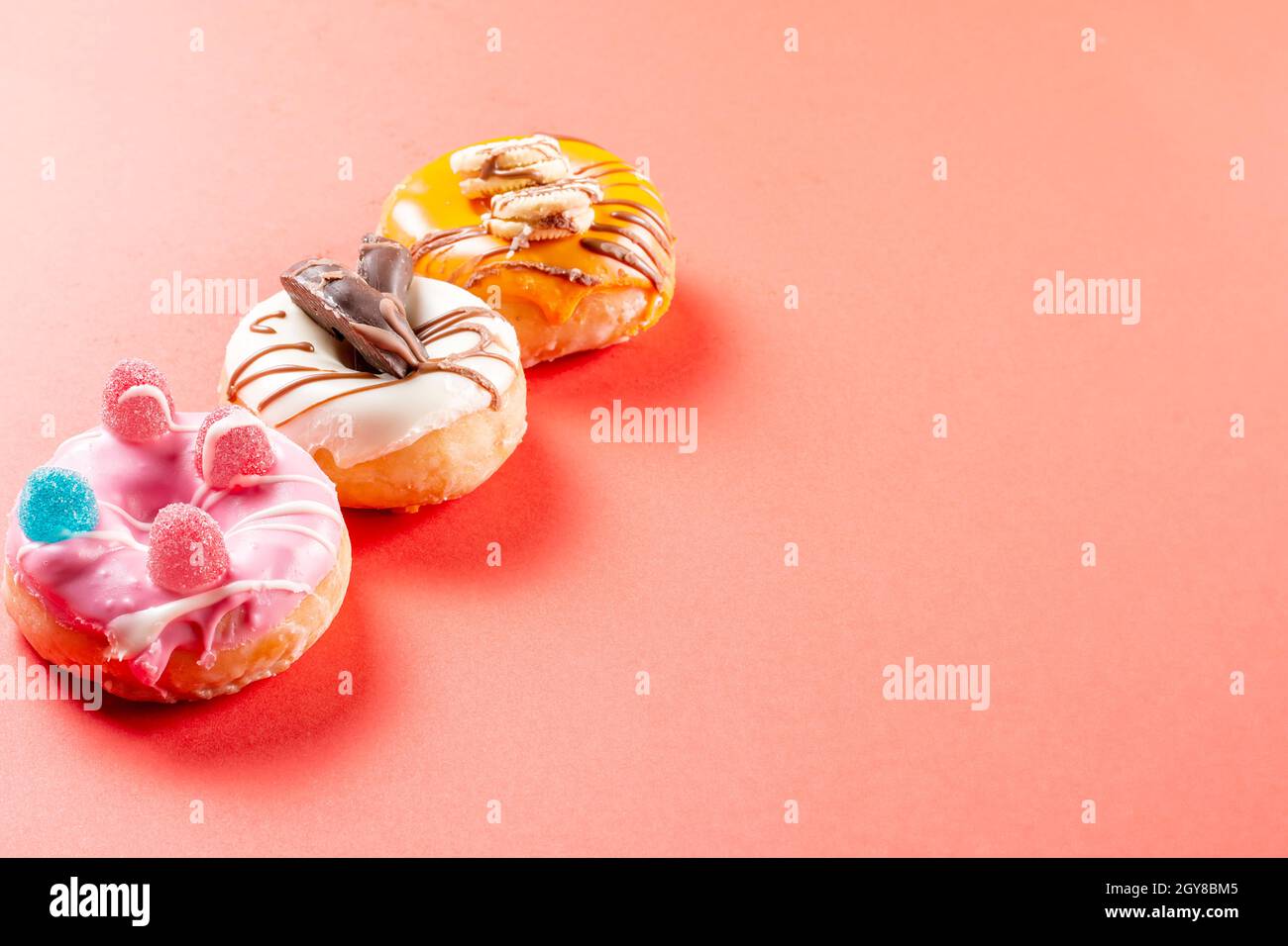 Foto von 3 Donuts, die mit Keksen und Jelly Beans dekoriert sind.die Donuts sind in Erdbeerschokolade, dunkle Schokolade und weiße Schokolade getaucht.Foto Stockfoto