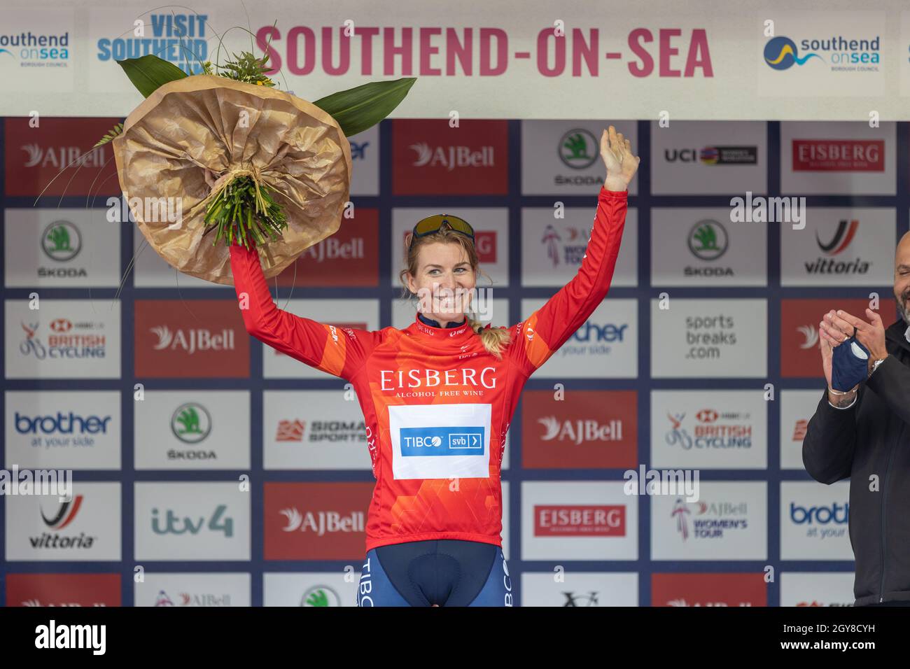 Southend on Sea, Großbritannien. Oktober 2021. Nina Kessler, Eisberg Sprints Trikotführerin feiert ihren ersten Platz am Ende der AJ Bell Women’s Tour in Southend-on-Sea. Sie trägt ein rotes EISBERG-Trikot und blaue VITUS-Shorts und steht auf dem zentralen Podium mit einem Blumenstrauß und einer Flasche Wein oder Champagner. Sponsorlogos wie Brother, Skoda, AJ Bell, Vittoria und Southend-on-Sea sind im Hintergrund zu sehen. Penelope Barritt/Alamy Live News Stockfoto