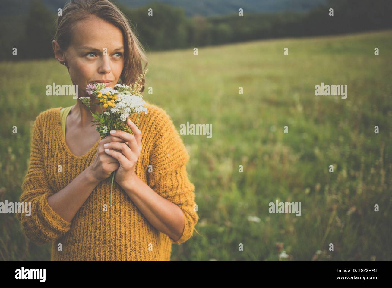 Schöne junge Frau im Freien mit einem Bouquet von wilden Blumen in einem Feld, die Natur zu genießen. Glückliche Frau auf Frühlingswiese Stockfoto