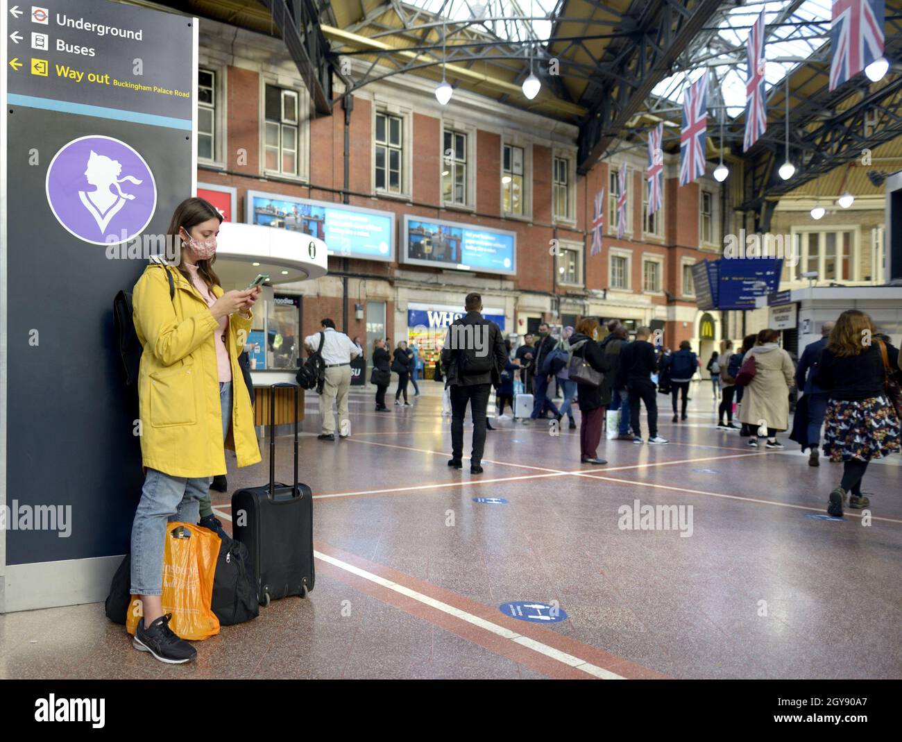 London, England, Großbritannien. Victoria Station: Junge Frau auf ihrem Mobiltelefon, mit COVID-Gesichtsmaske, Oktober 2021 Stockfoto