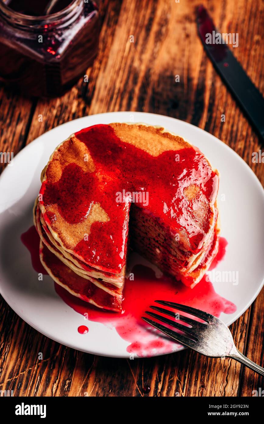Stapel von amerikanischen Pfannkuchen mit roten Beeren Marmelade auf der Platte über rustikale Oberfläche Stockfoto