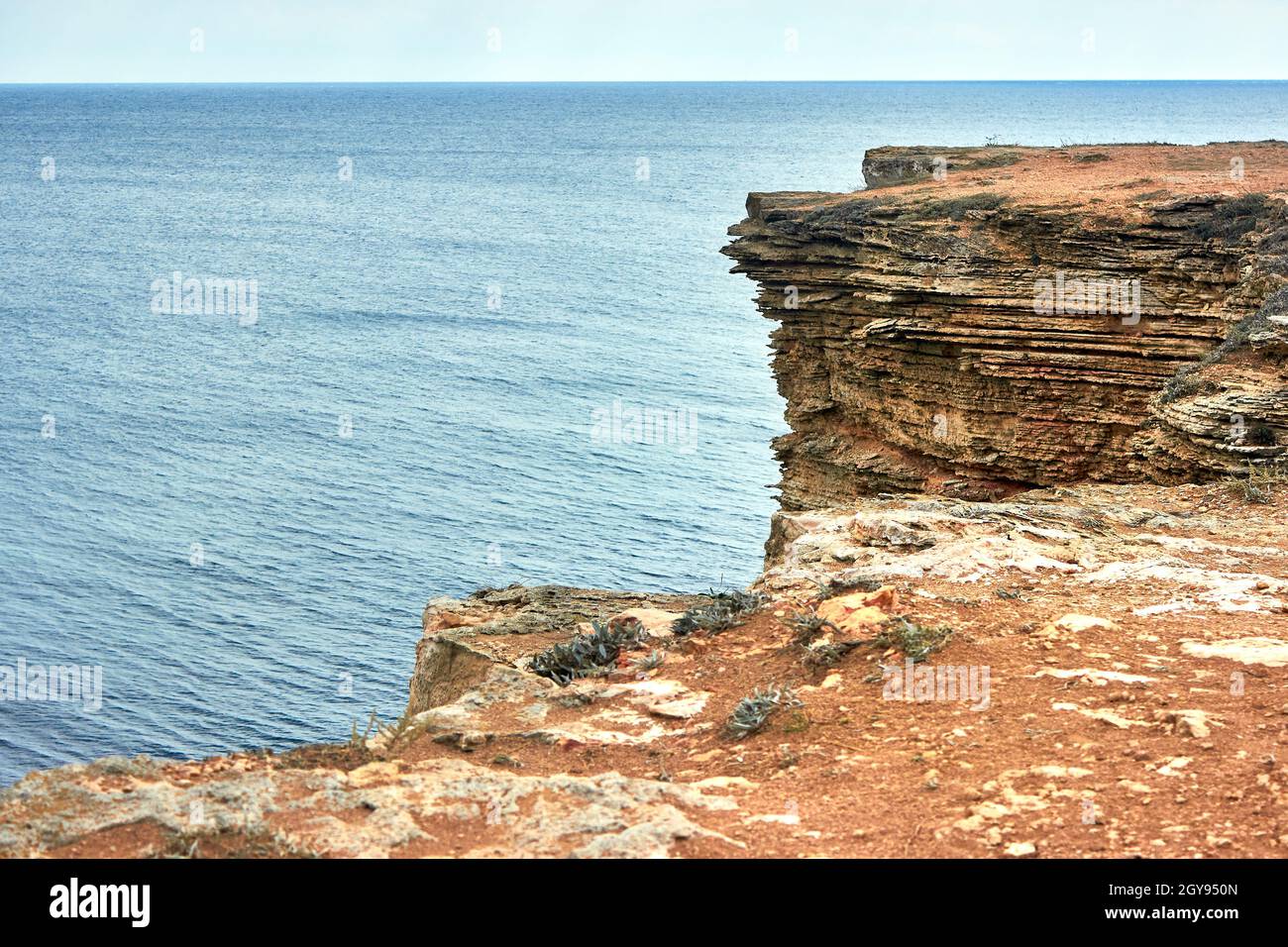 Gelbe felsige Küste, Klippe. Blaues tiefes ruhiges Meer. Ruhiger blauer Himmel. Der westliche Teil der Krim, Kap Tarkhankut. Wunderschöne Naturlandschaft. Stockfoto