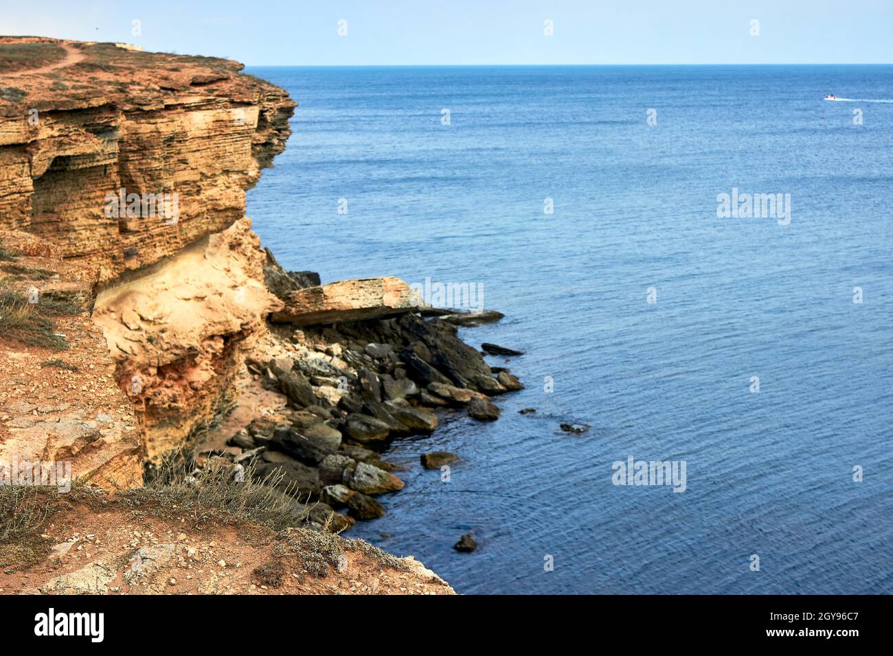 Gelbe felsige Küste, Klippe. Blaues tiefes ruhiges Meer. Ruhiger blauer Himmel. Blick von oben auf das plätschernde Meer. Der westliche Teil der Krim, Kap Tarkhankut. Stockfoto