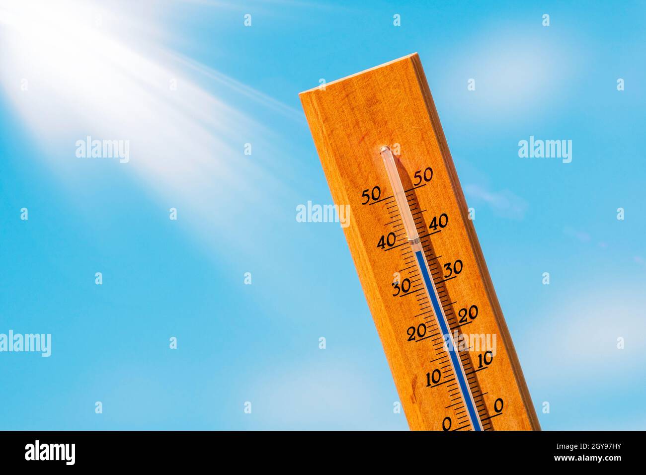 Thermometer mit einer Hochtemperaturanzeige auf einer Skala, vor einem Hintergrund von heller Sonne und einem blauen Himmel mit Wolken. Das Konzept der heißen, gefährlichen w Stockfoto