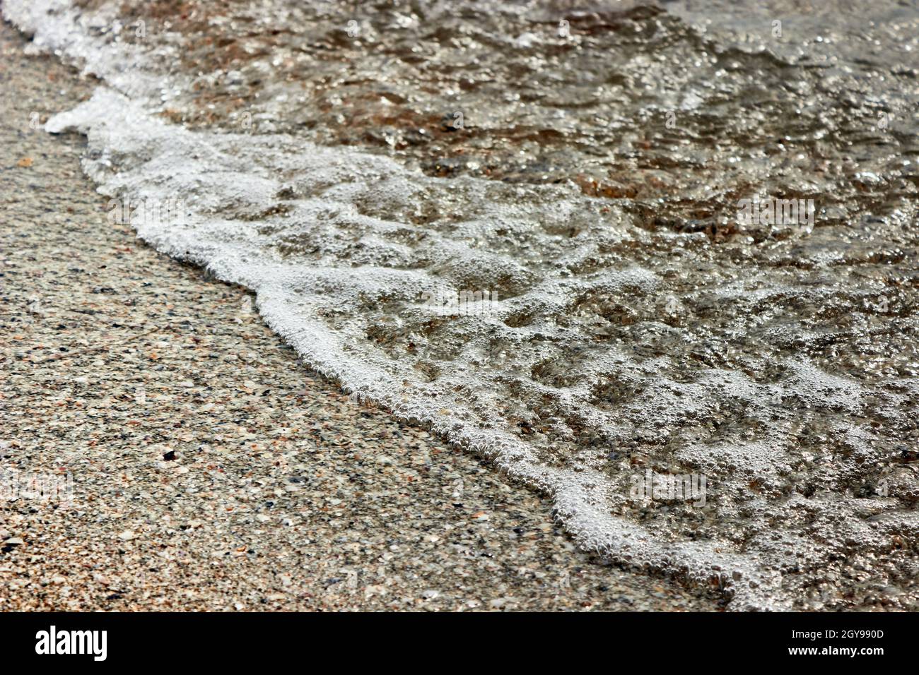 Meeresschaum auf Strandsand mit klarem Wasser. Sand Beach Und Sea Foam Makro Mit Engem Fokus Hintergrund. Sommerhintergrund. Horizontales Foto. Stockfoto