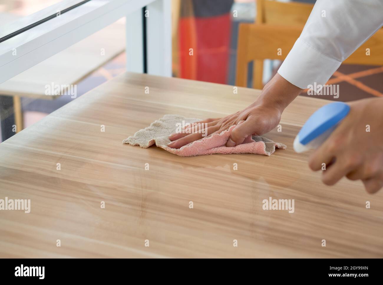 Die Hand des Kellners aus der Nähe Verwenden Sie einen flüssigen Reiniger und ein Handtuch, um die Flecken auf dem Tisch abzuwischen. Stockfoto