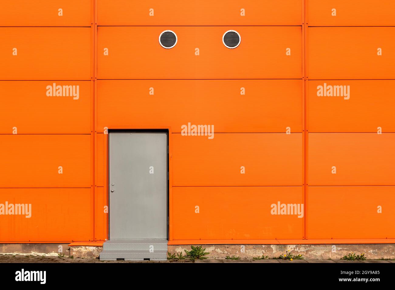 Industrielle orange Gebäudewand mit Metalltüren Stockfoto