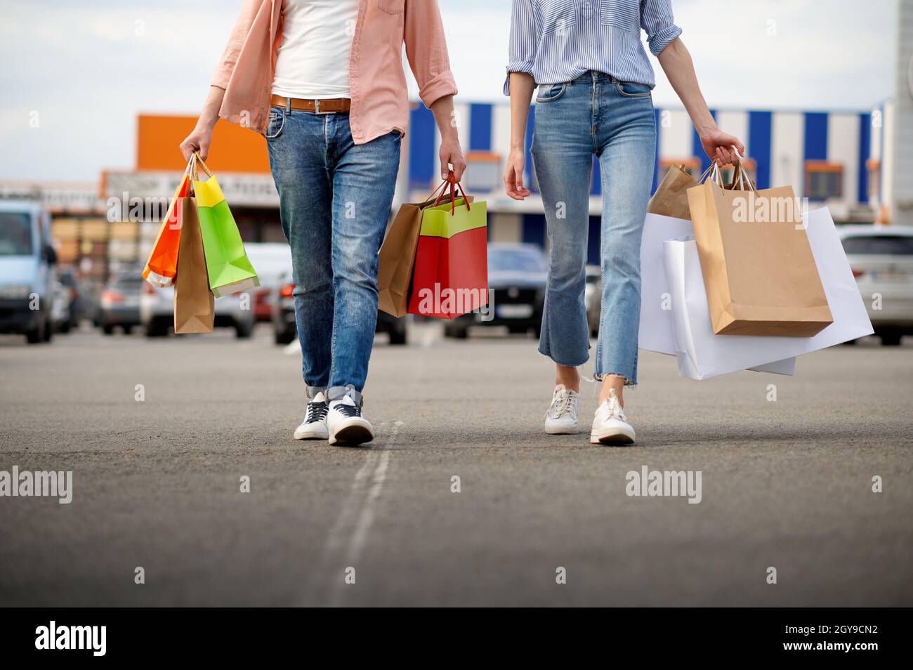 Mann und Frau mit Papptüten auf dem Parkplatz im Supermarkt. Zufriedene Kunden mit Einkäufen im Einkaufszentrum, Fahrzeuge im Hintergrund Stockfoto