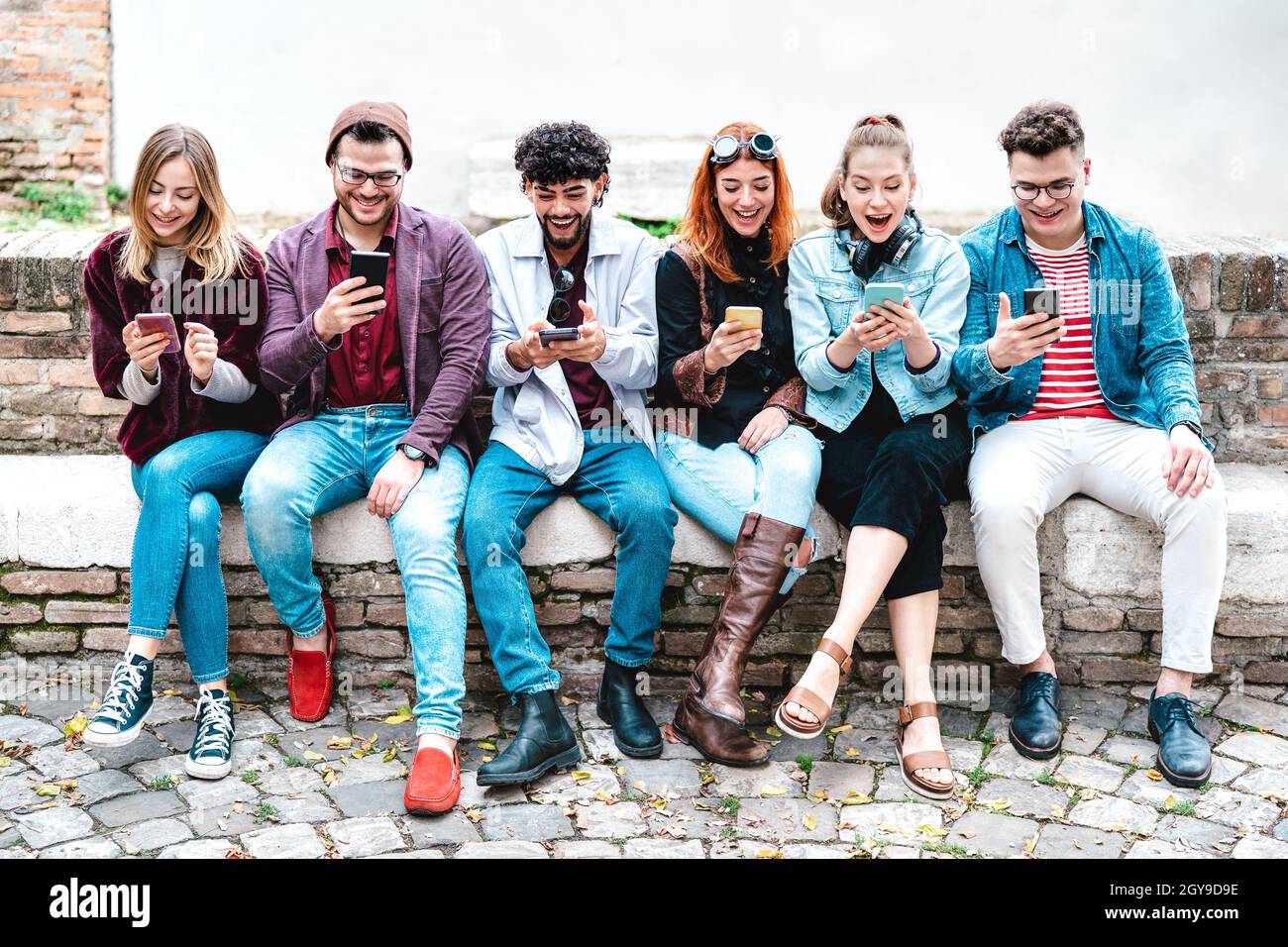 Glückliche Freunde, die während der Hochschulferien ein Smartphone nutzen – Menschen, die Trendinhalte mit mobilen Smartphones teilen – Technologiekonzept Stockfoto