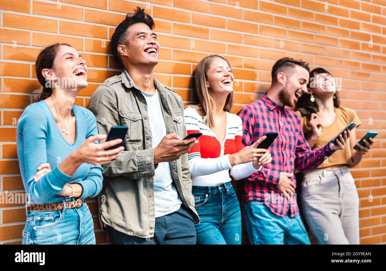 Multikulturelle Freunde lachen mit dem Smartphone an der Wand des Universitätscampus - Junge Menschen, die von mobilen Smartphones süchtig sind Stockfoto